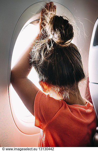 Rear view of girl looking through airplane window