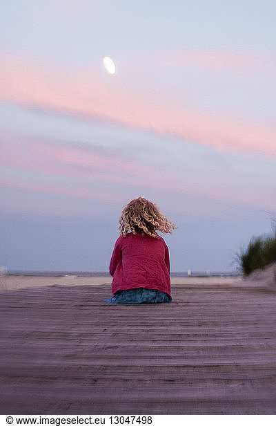 Rear view of girl sitting at beach against sky during sunset, Rear view of girl sitting at beach against sky during sunset