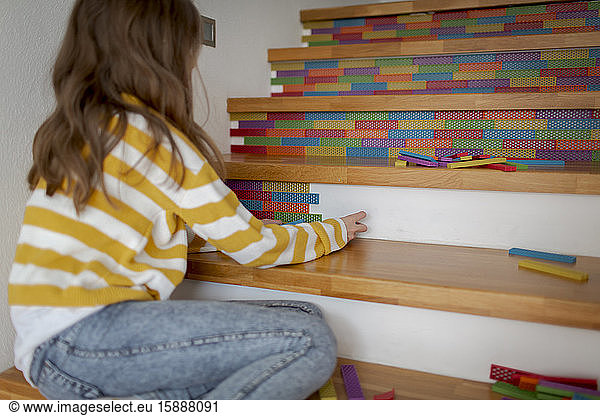 Rear view of girl sitting on stairs and playing with wooden blocks