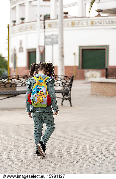 Rear view of girl walking with backpack and mask on square