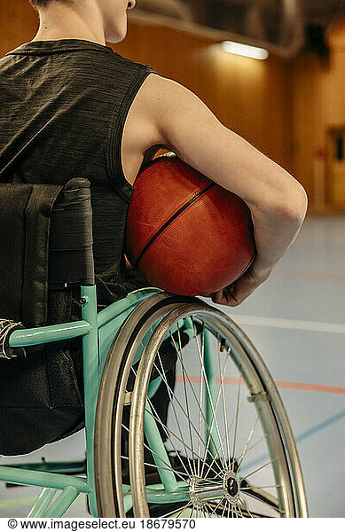 Rear view of girl with disability sitting on wheelchair while holding basketball at sports court