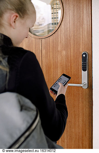 Rear view of girl with smart phone unlocking door
