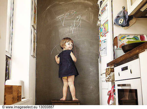Rear view of girl writing on wall while standing on stool at home