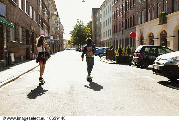 Rear view of girls skateboarding on street amidst buildings