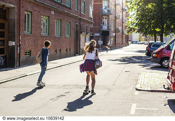 Rear view of girls skateboarding on street by buildings