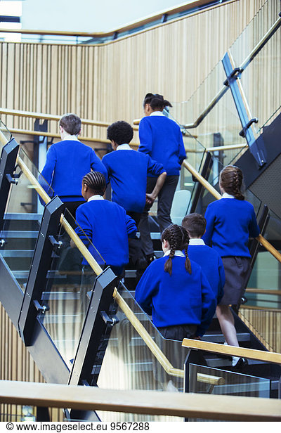 Rear view of group of pupils wearing blue school uniforms walking up stairs in school