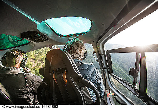 Rear view of helicopter pilot flying low through forested mountains.