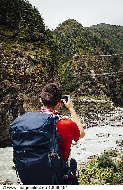 Rear view of hiker with backpack photographing river amidst mountains at Sagarmatha National Park