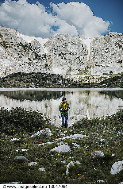 Rear view of hiker with backpack standing at lakeshore against Medicine Bow Mountains