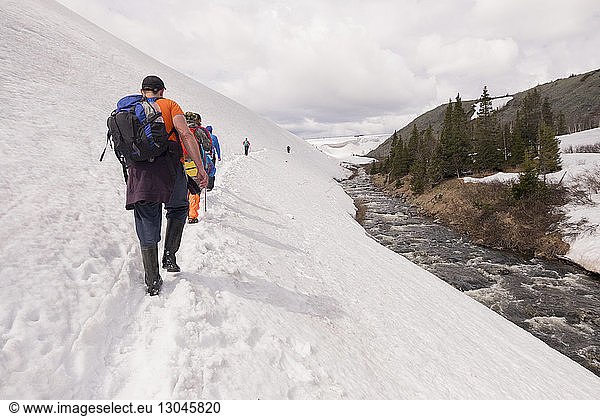 Rear view of hikers walking on snow covered hill against cloudy sky