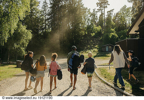 Rear view of kids walking on footpath with counselors at summer camp