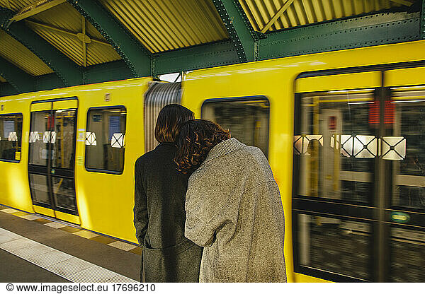 Rear view of lesbian couple standing at railroad station against yellow train