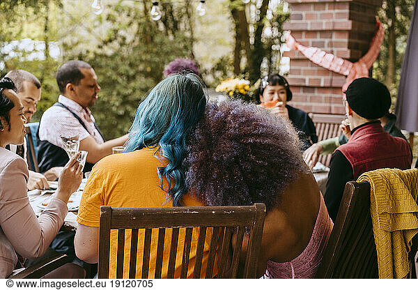 Rear view of LGBTQ friends sitting together during dinner party in back yard