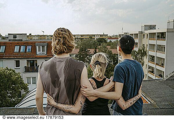 Rear view of male and female friends standing with arms around on rooftop