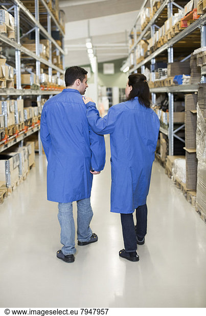 Rear view of male and female technicians walking in factory