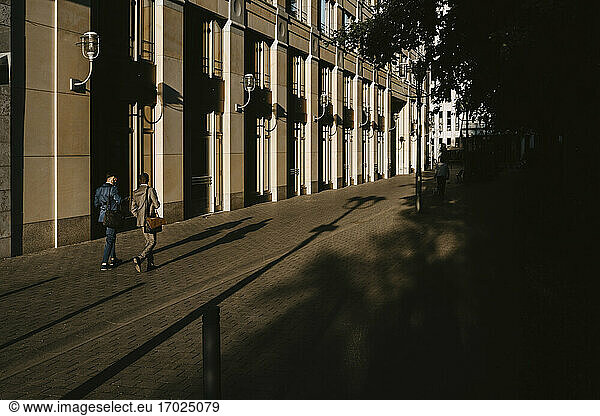 Rear view of male colleagues walking while discussing on footpath in city