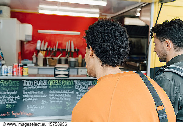 Rear view of male friends looking at menu of food truck in city