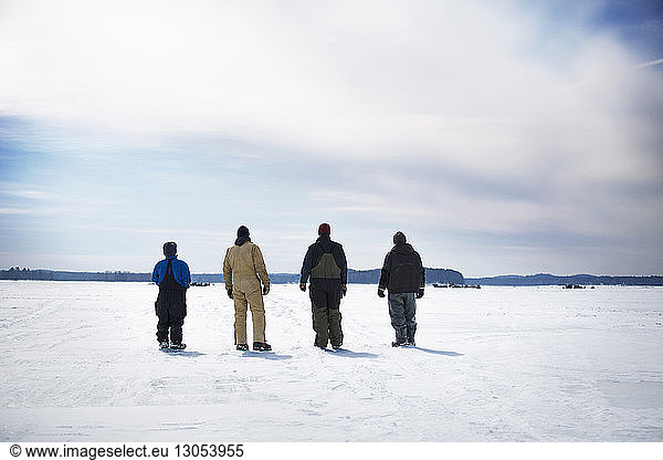 Rear view of male friends standing on frozen lake against cloudy sky