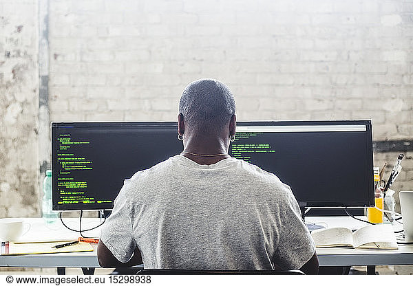 Rear view of male IT expert using computer while coding at creative workplace