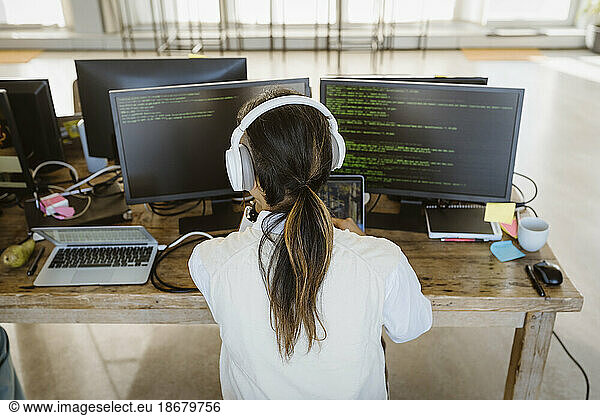 Rear view of male programmer working on computer at desk in creative office