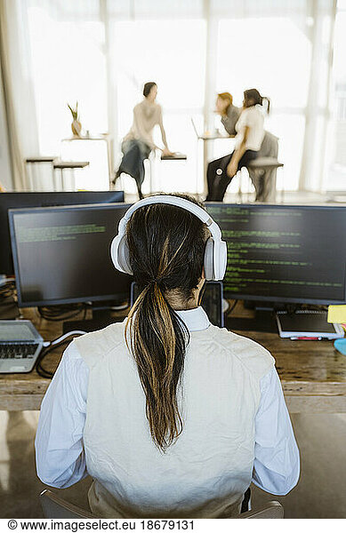 Rear view of male programmer working on computer at desk in office