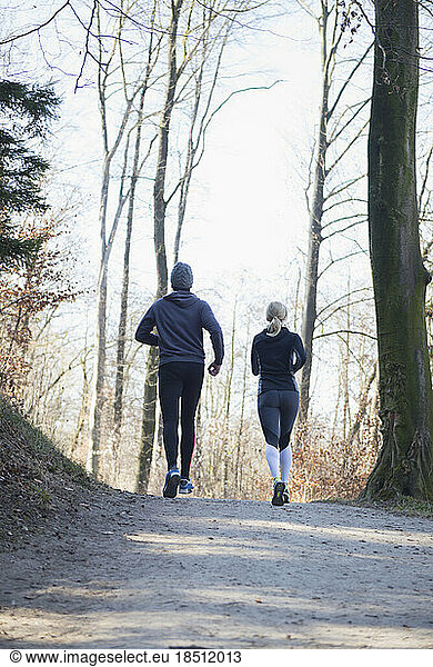 Rear view of man and woman jogging on fitness trail in forest