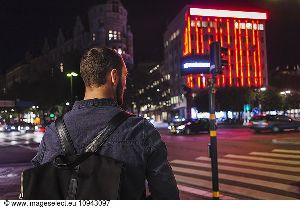 Rear view of man carrying backpack while standing on city street at night