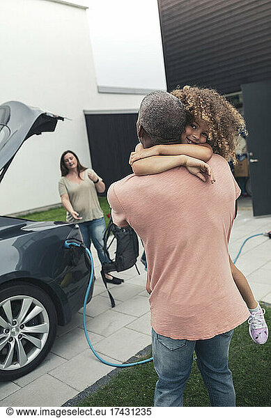 Rear view of man carrying daughter while standing by electric car