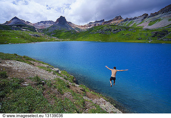 Rear view of man diving into lake by mountains against cloudy sky