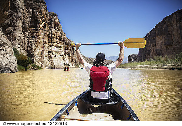 Rear view of man holding oar while sitting in boat on river at Big Bend National Park