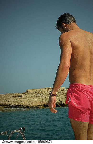 Rear view of man in pink swimming trunks standing by sea on sunny day