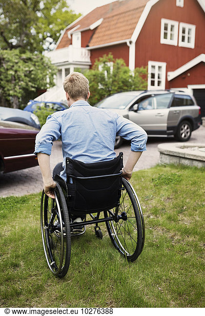Rear view of man in wheelchair at yard