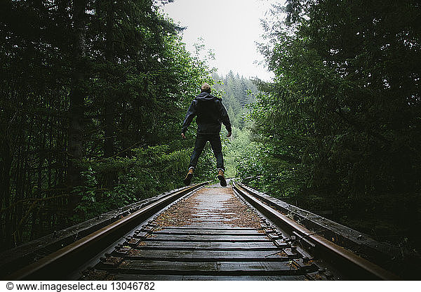 Rear view of man jumping on railway tracks amidst trees