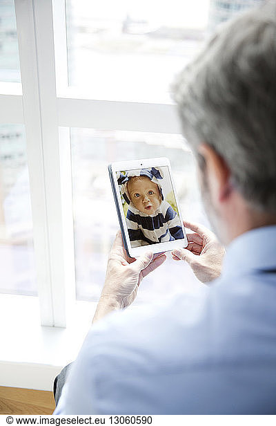 Rear view of man looking at baby's photograph in smart phone