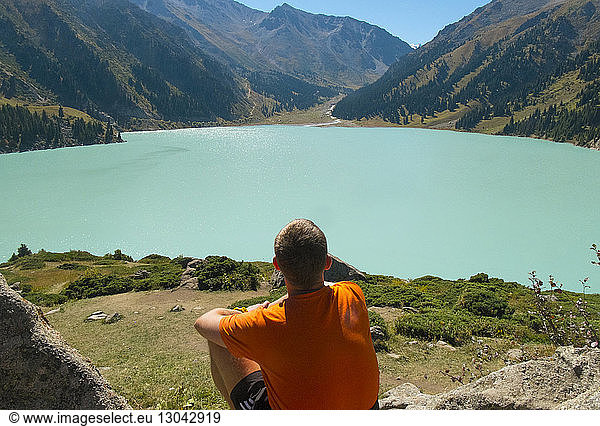 Rear view of man looking at view while sitting at lakeshore