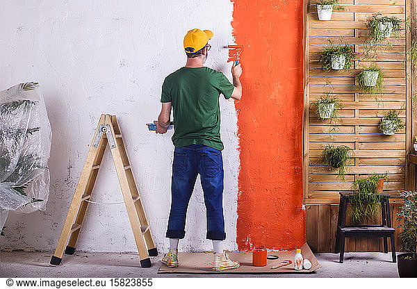 Rear view of man painting orange wall in his garden terrace