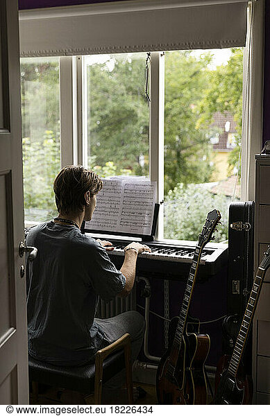 Rear view of man reading music note while practicing piano at home