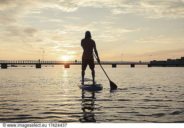 Rear view of man rowing paddleboard in sea