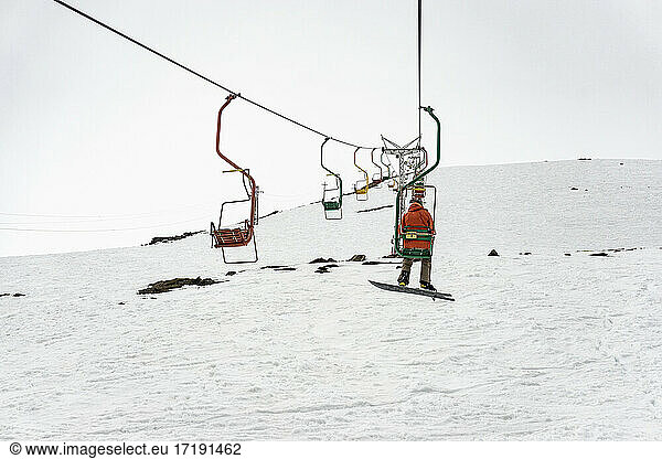 Rear view of man sitting on ski lift over snowfield against clear sky