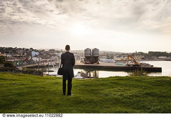 Rear view of man standing on grassy hill by industry