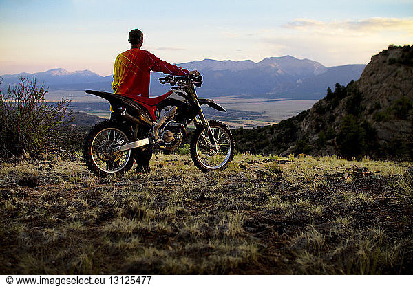 Rear view of man standing with dirt bike on field