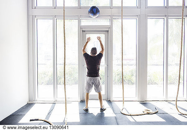 Rear view of man throwing medicine ball while exercising in crossfit gym