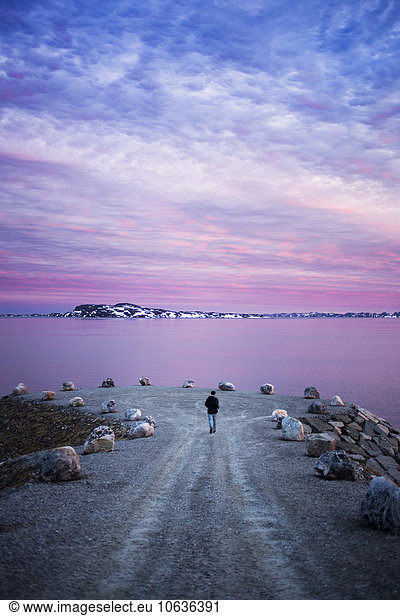 Rear view of man walking on groyne leading towards sea during sunset