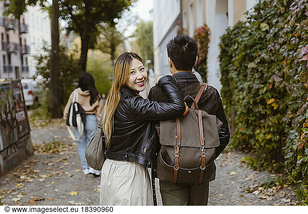 Rear view of man walking with female friend looking over shoulder on sidewalk