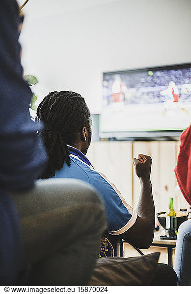 Rear view of man watching soccer match with friend at home