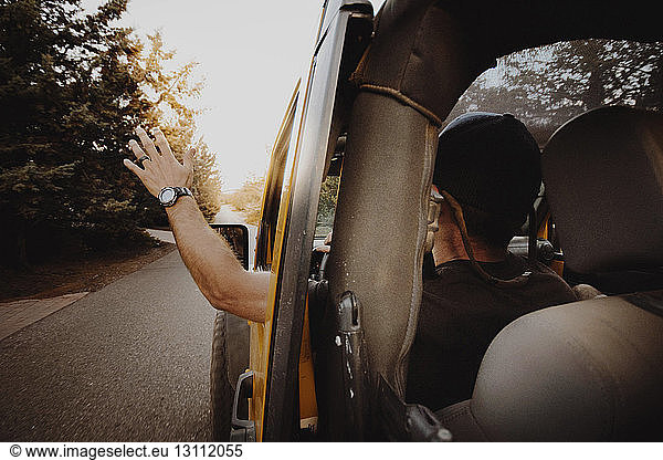Rear view of man waving through off-road vehicle window while driving on road