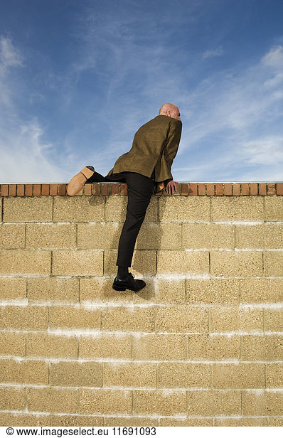 Rear view of man wearing a suit climbing over yellow brick wall.