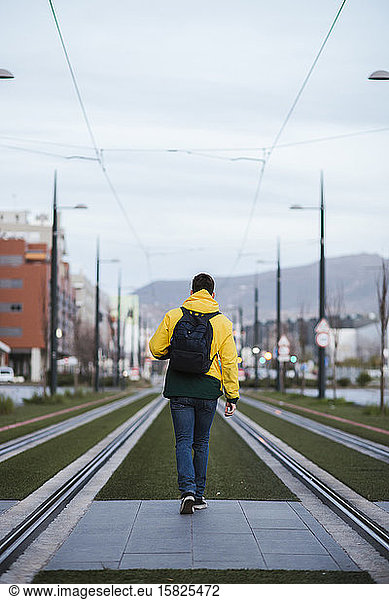 Rear view of man with backpack in the city on tram tracks