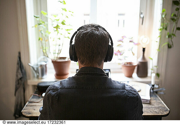Rear view of man with headphones working on laptop at home during pandemic