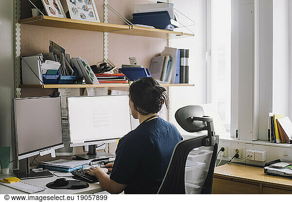Rear view of mature female nurse working on computer in clinic